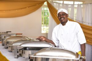 A cheerful chef stands by chafing dishes in a Nairobi hotel buffet setting.