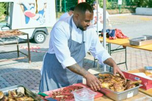 Professional chef arranging grilled chicken at outdoor food event.